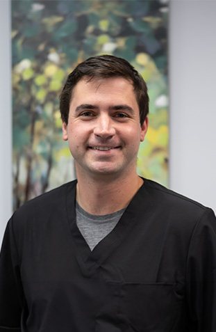The image shows a man wearing scrubs, standing indoors with a smiling expression, likely posing for an official portrait.