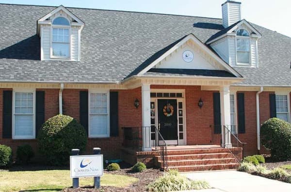 The image shows a two-story residential house with a dark roof, white trim around the windows and doors, and a brick facade. There is a sign in front of the house that reads  Lakewood.