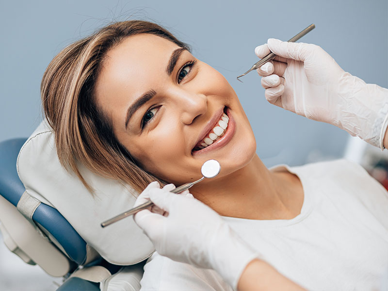 A woman receiving dental care, smiling with her eyes closed while a hygienist works on her teeth.