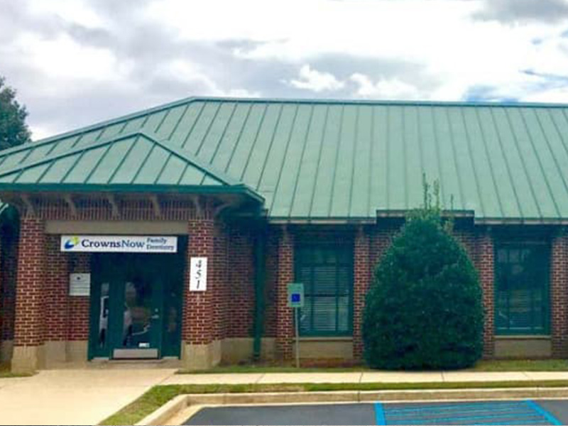 The image depicts a building with a green roof, featuring a sign that reads  CrownNow,  and there s a tree in the foreground.
