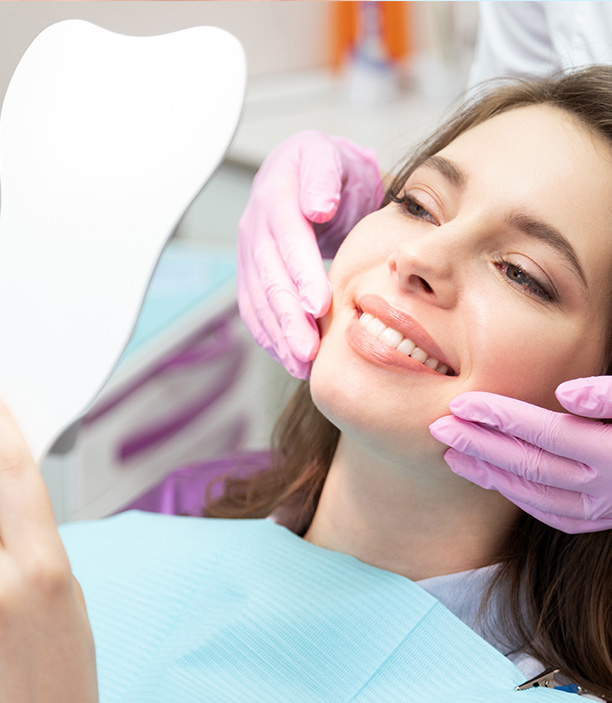 This is an image of a dental care setting where a woman is seated in a dentist's chair, receiving treatment, with a dental mirror and a professional attendant assisting her.