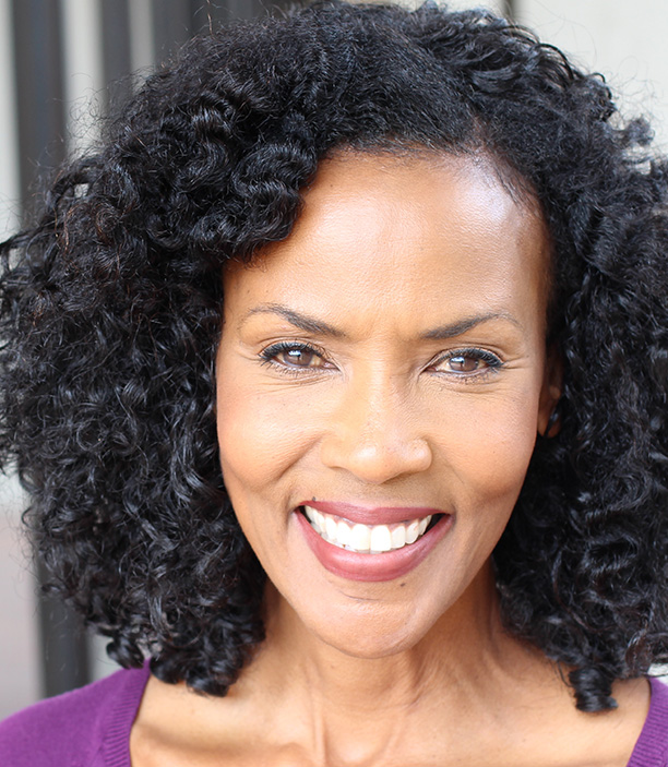 The image shows a woman with curly hair, wearing a purple top and smiling at the camera.