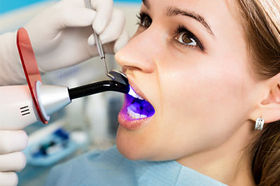 A woman is seated in a dental chair, receiving treatment with a dental device attached to her mouth.