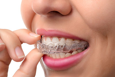 A woman with a toothy smile is holding a piece of dental floss between her teeth, capturing the moment before she brushes.