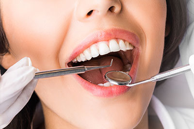 A woman in a dental chair receiving dental treatment with an open mouth and dental instruments visible.