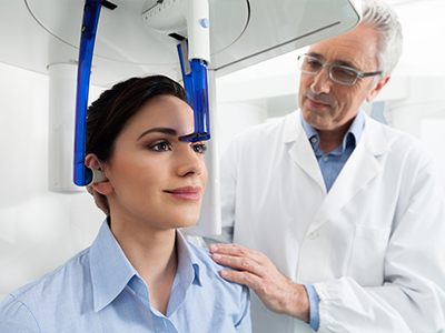 A medical professional is demonstrating a 3D scanner device to a seated patient in a clinical setting.