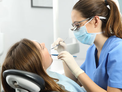 A dental hygienist is performing a cleaning procedure on a patient s teeth while wearing protective gear.