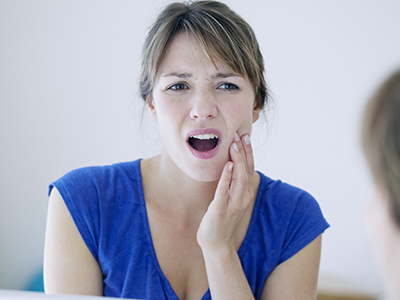 A young woman with a surprised expression, holding her hand to her mouth, in front of a mirror.