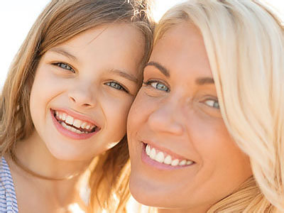 The image shows a woman and a young girl smiling at the camera, with the woman s face partially obscured by the child.