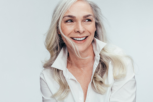 The image is a portrait of an adult woman with blonde hair, wearing a white top and smiling at the camera.