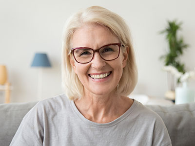 A woman with short blonde hair, wearing glasses and a casual top, is smiling at the camera.