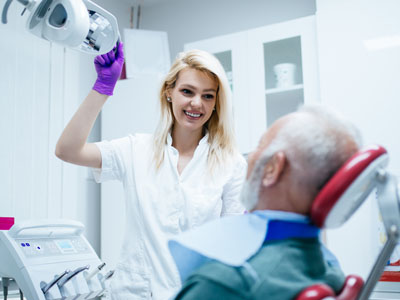 A dental professional attends to a patient in a dental chair, with medical equipment in the background.