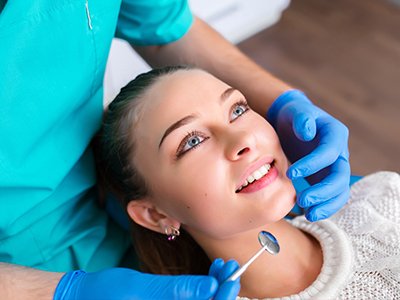 A dental professional is performing a procedure on a patient's teeth, with the patient smiling and looking at the camera.