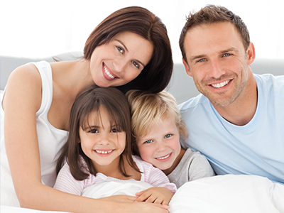 A family of four posing in bed, with a smiling man, woman, and two children.