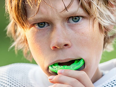 The image shows a young person with blonde hair, wearing a football jersey and holding a toothbrush to their mouth.